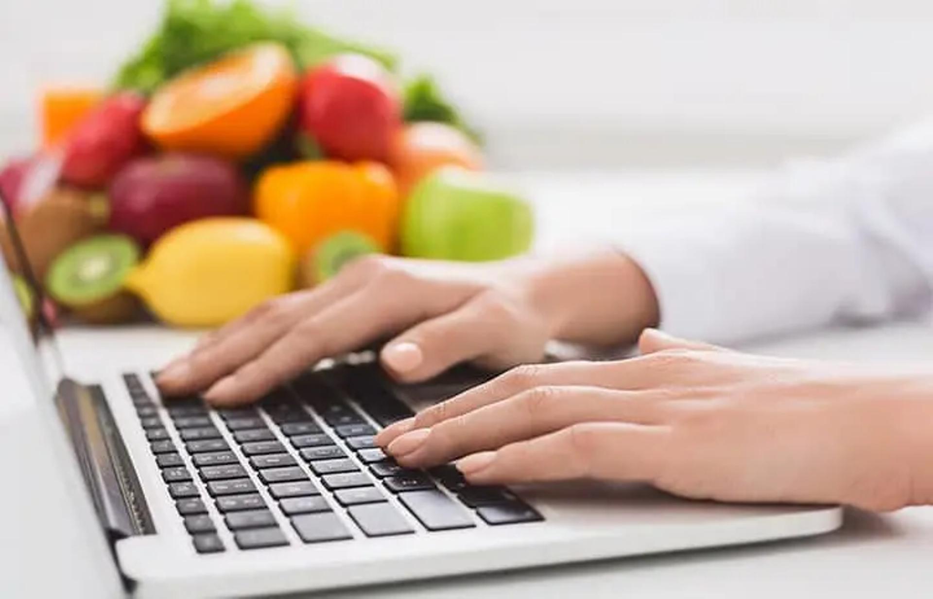 Hands on keyboard with fruits and vegetables in the background